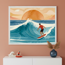 Modern room with a terracotta wall and white dresser. A large white-framed illustration of a surfer on a big blue wave with a setting orange sun hangs above. On the dresser, a white wave sculpture, a surfer cutout, and a blue vase with pampas grass.