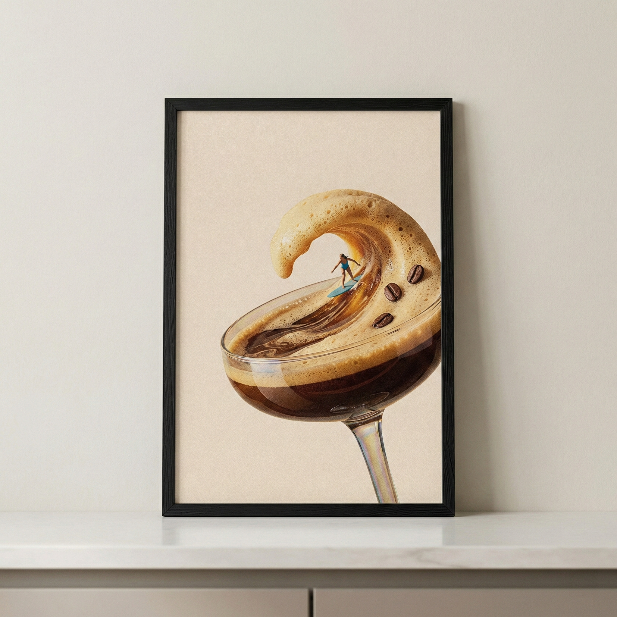 A framed art print featuring a surreal scene is displayed against a neutral-toned wall on a white surface. The image within the black frame shows a tall-stemmed coupe glass containing a dark coffee-colored liquid. The thick, frothy golden-brown foam on top of the liquid rises and curls upward, taking the shape of a large, cresting ocean wave. Inside the curve of this foam wave, a miniature surfer on a small blue surfboard rides the espresso froth. 