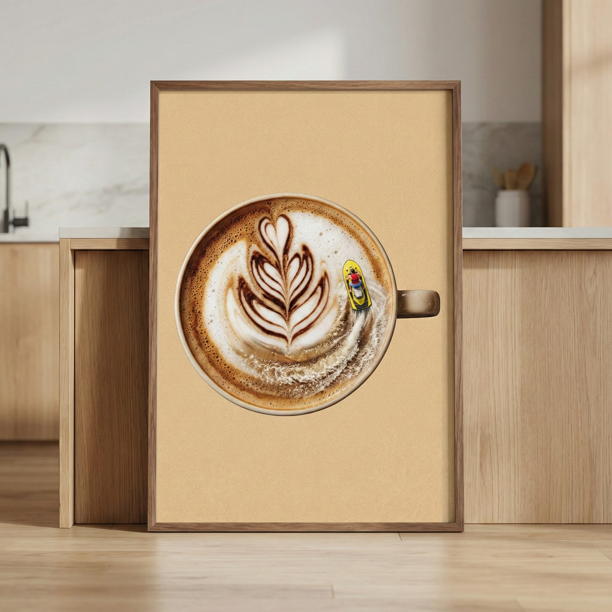 A framed artwork is shown leaning against a wooden cabinet in a contemporary kitchen. The central subject of the art is a top-down view of a round cup of coffee. The coffee features intricate white latte art in a leaf-like, symmetrical pattern. Next to this pattern, a tiny figure on a bright yellow personal watercraft is shown moving across the surface, leaving a froamy white wake in the brown liquid. The artwork has a solid, warm beige background and is held within a simple light wood frame. 