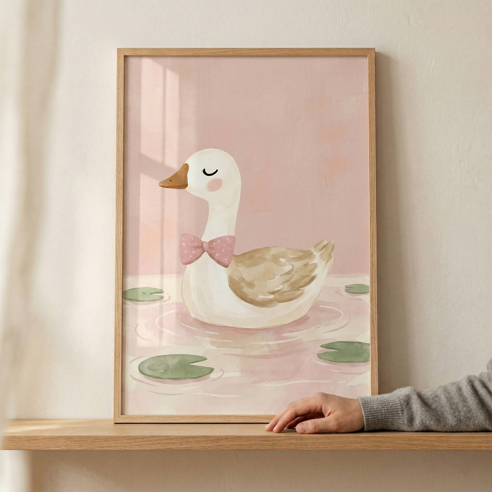 A charming vertical illustration features a stylized white duck with a soft brown wing swimming peacefully on a pale pink pond. The duck has a small orange-brown beak, a closed eye with a fine eyelash, a rosy pink cheek, and a pink polka-dot bow tie around its neck. Several muted green lily pads float on the water's surface, which is accented with delicate ripples. The entire scene is set against a soft, warm pink background.