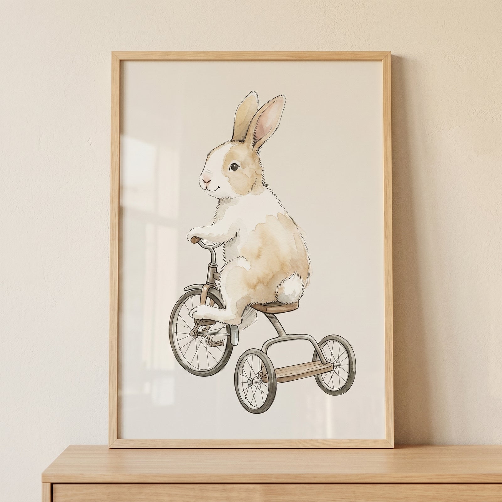 Framed tan white riding bunny wall art shows a watercolor-style rabbit on a tricycle leaning against a neutral wall.