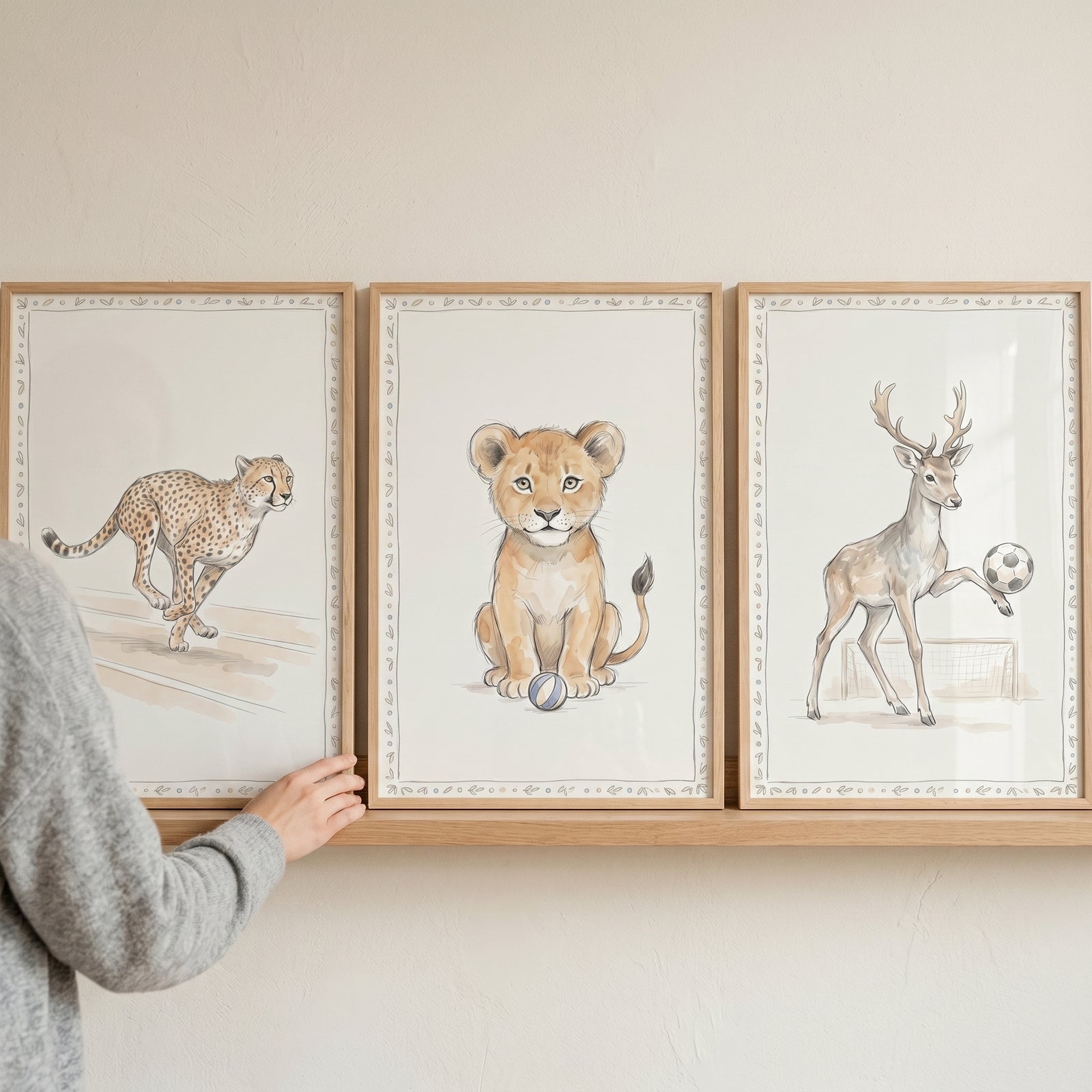 Taupe watercolor sporting animals wall art set of 3 with a running cheetah, lion cub, and deer playing soccer.