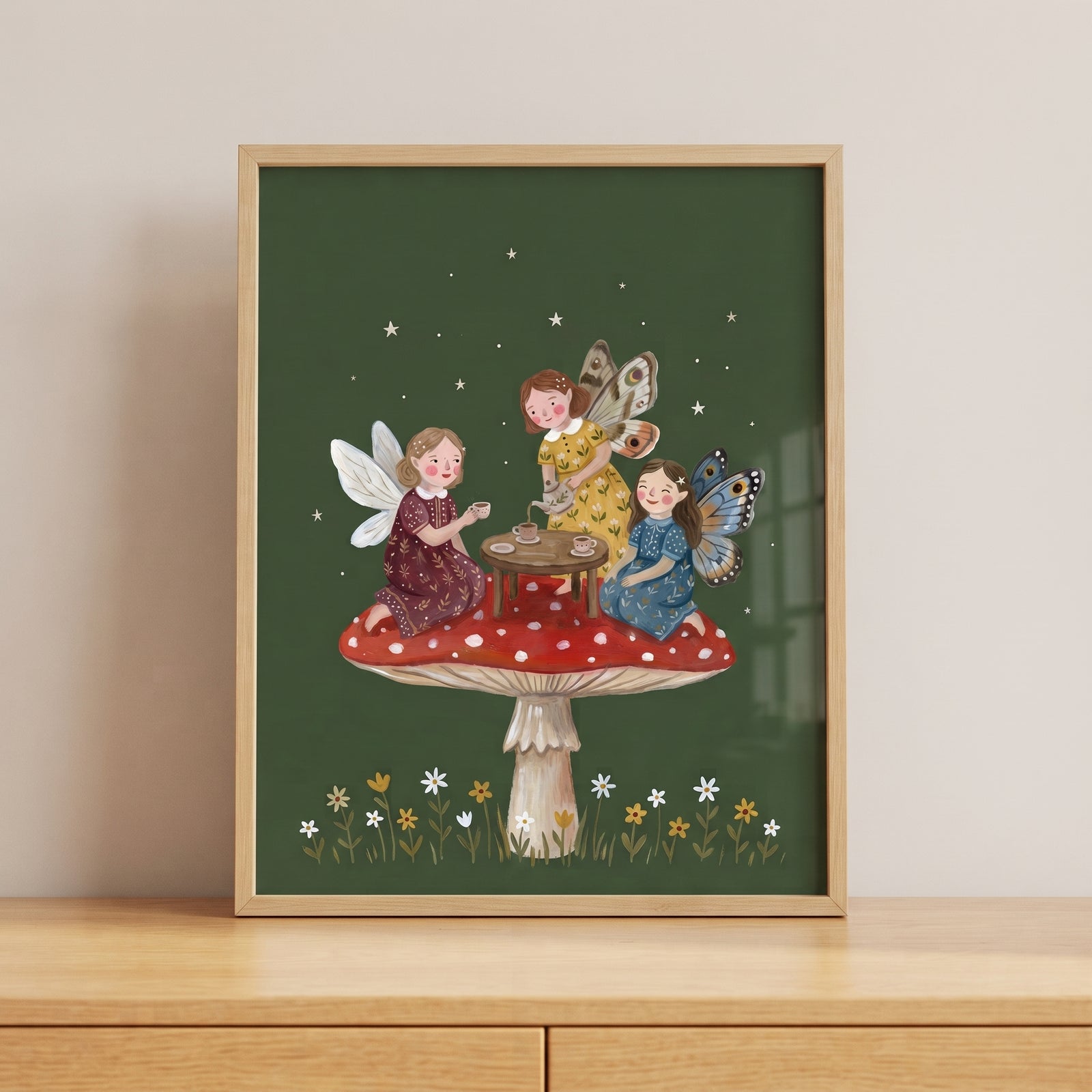 Three winged figures share tea on a red mushroom in this tea party mushroom fairies wall art with stars and flowers.