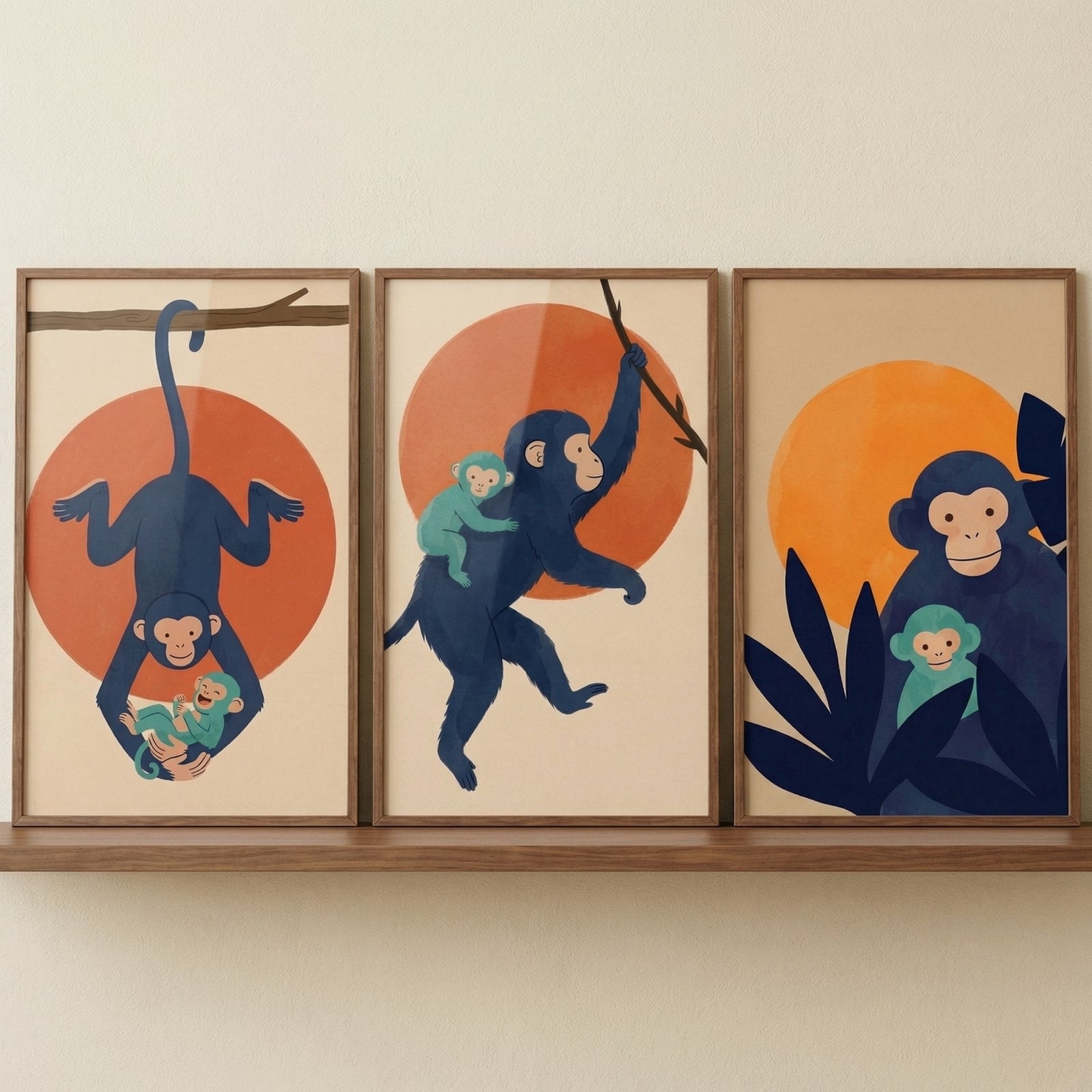 A triptych of three framed art pieces sits on a wooden shelf against a neutral-colored wall. The illustrations use a minimalist, modern aesthetic with flat, bold colors. Each piece features a large navy blue monkey and a smaller teal baby monkey set against a prominent orange circular shape.
