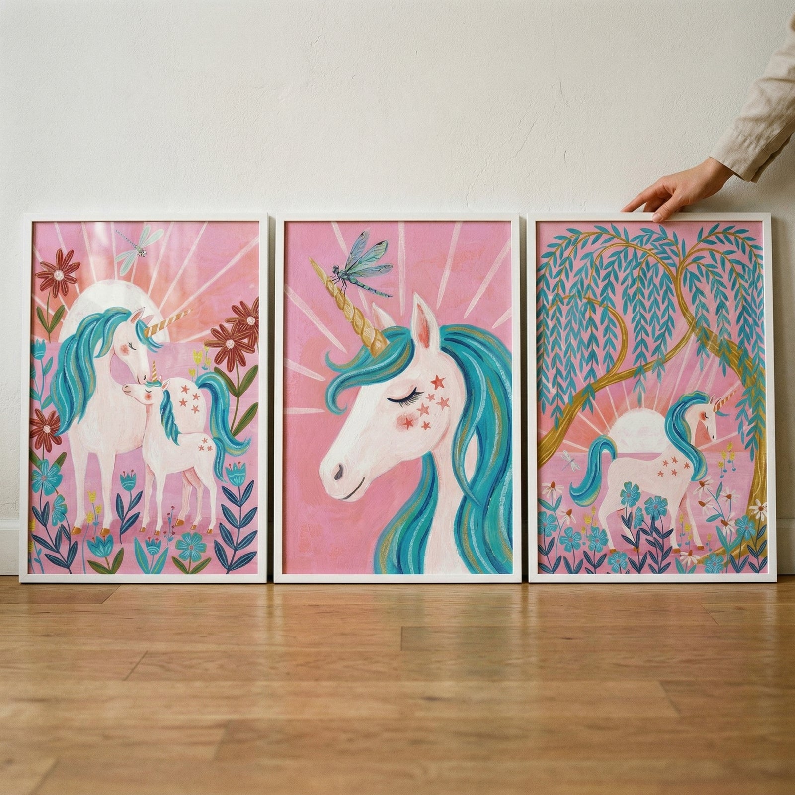 Teal mane white unicorn wall art set of 3 on a wooden floor featuring pink backgrounds, flowers, and dragonflies.
