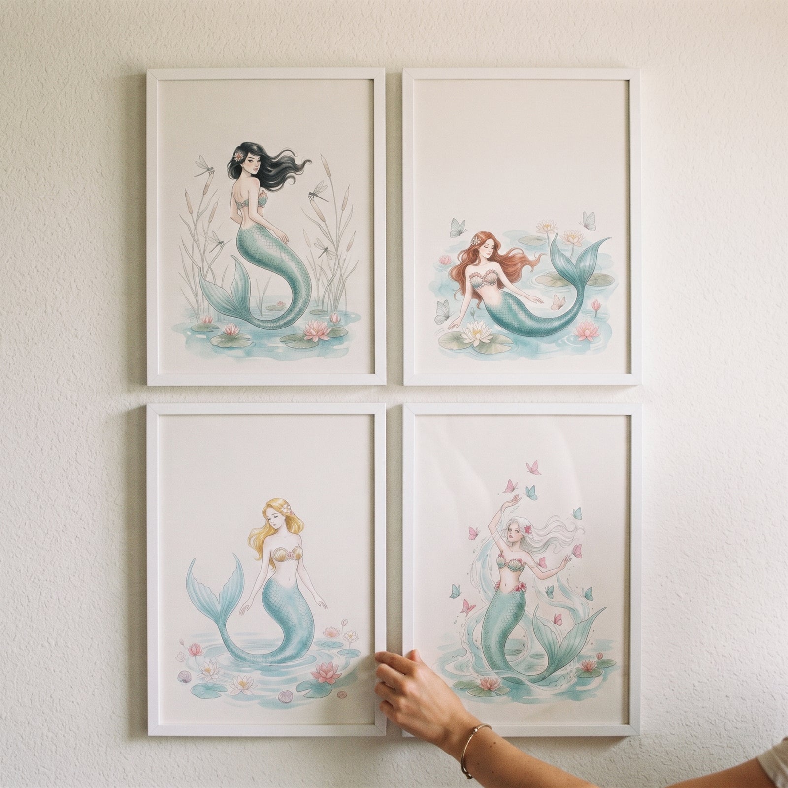 Teal tail watercolor mermaid wall art set of 4 in white frames being adjusted by a hand on a plain wall.