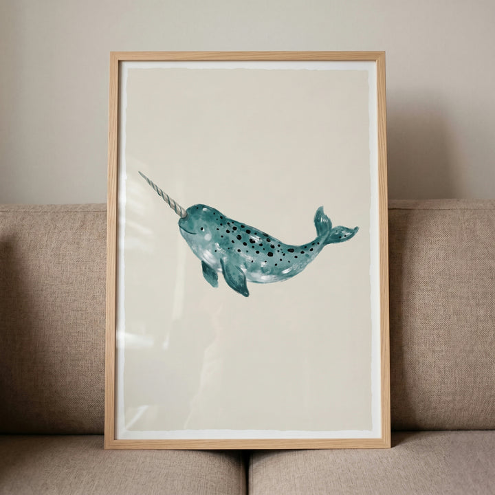 Teal watercolor narwhal wall art with a long tusk and dark spots, framed in light wood against a beige sofa.