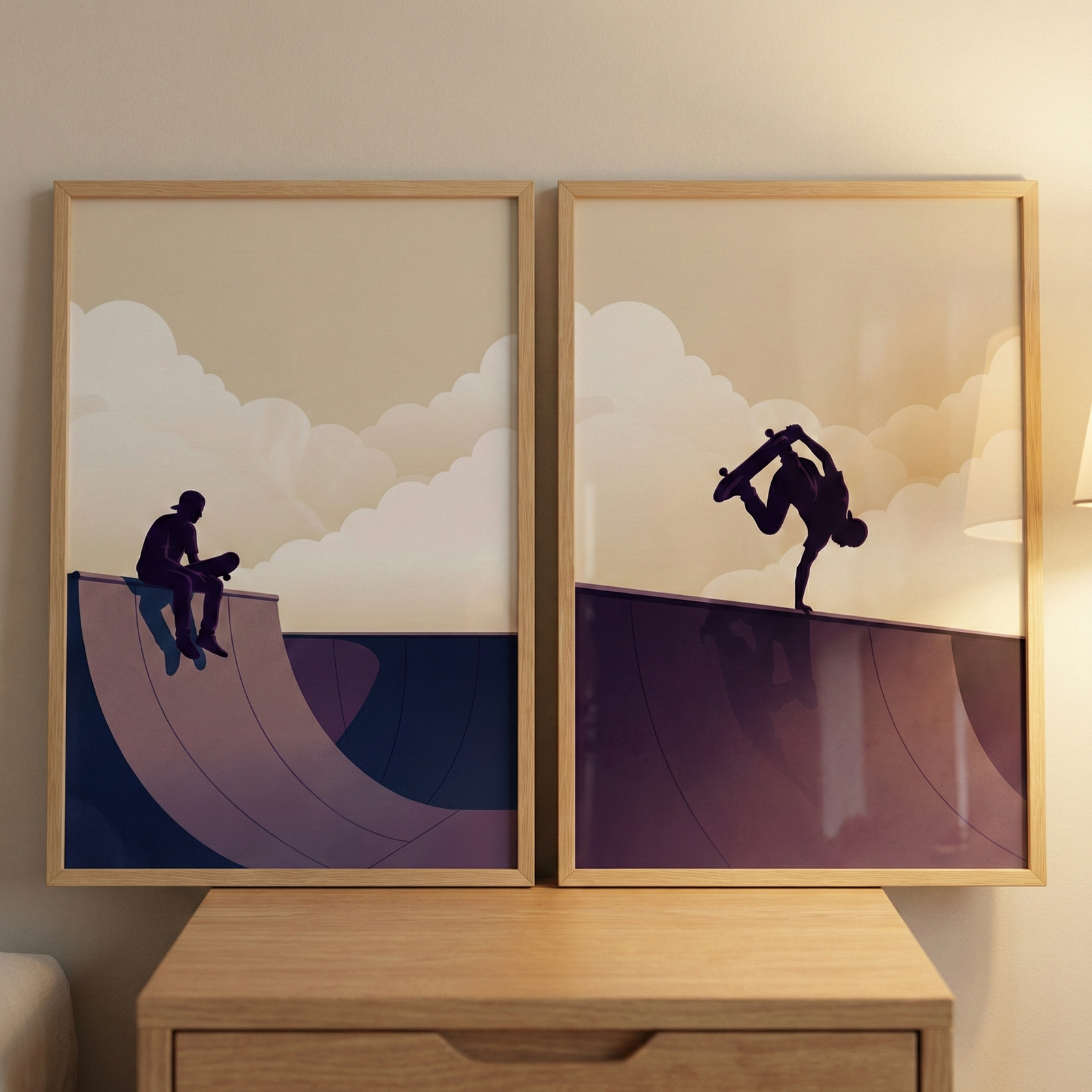 Two framed minimalist illustrations are placed side-by-side on a wooden dresser. The left image shows a silhouette of a person sitting on the edge of a skate park ramp, while the right image depicts a silhouette of a skateboarder performing a handplant trick. Both pieces feature a muted color palette of purple, navy, and cream, with stylized clouds in the background. The prints are presented in light-colored wooden frames.