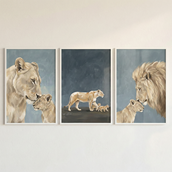 A set of three vertically-oriented framed illustrations featuring a lion family, displayed side-by-side on a neutral wall. The left frame shows a close-up profile of a lioness tenderly touching her nose to a small cub's head. The center frame depicts a lioness walking across a dark surface followed by two small cubs against a dark blue background. The right frame features a male lion with a full mane gently touching his nose to a cub's head. The art style is soft and textured in muted tones.