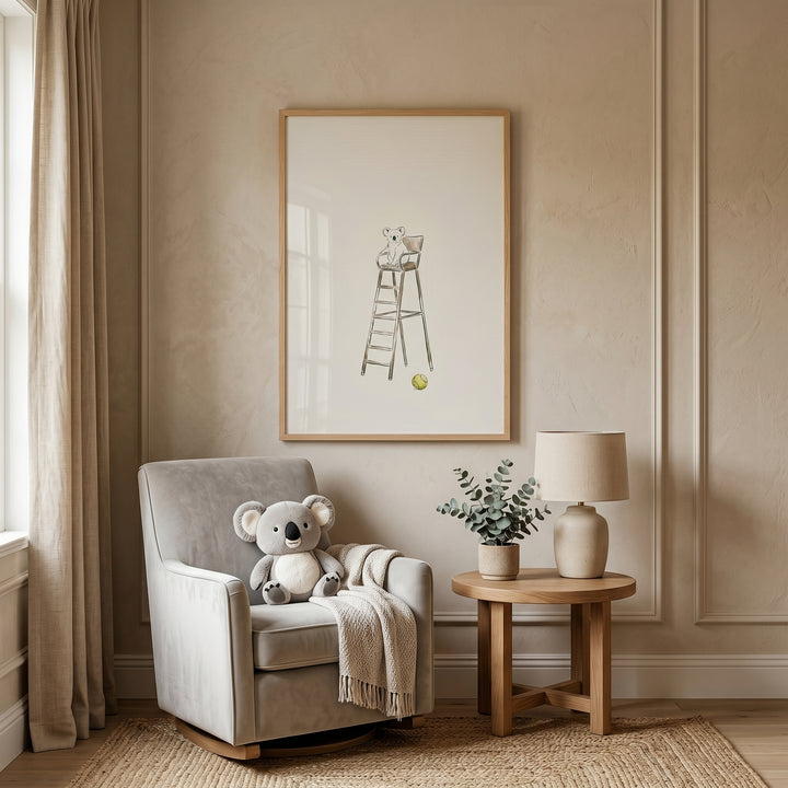 Grey armchair with a plush toy sits below tennis ball illustration koala wall art in a room with a lamp and side table.