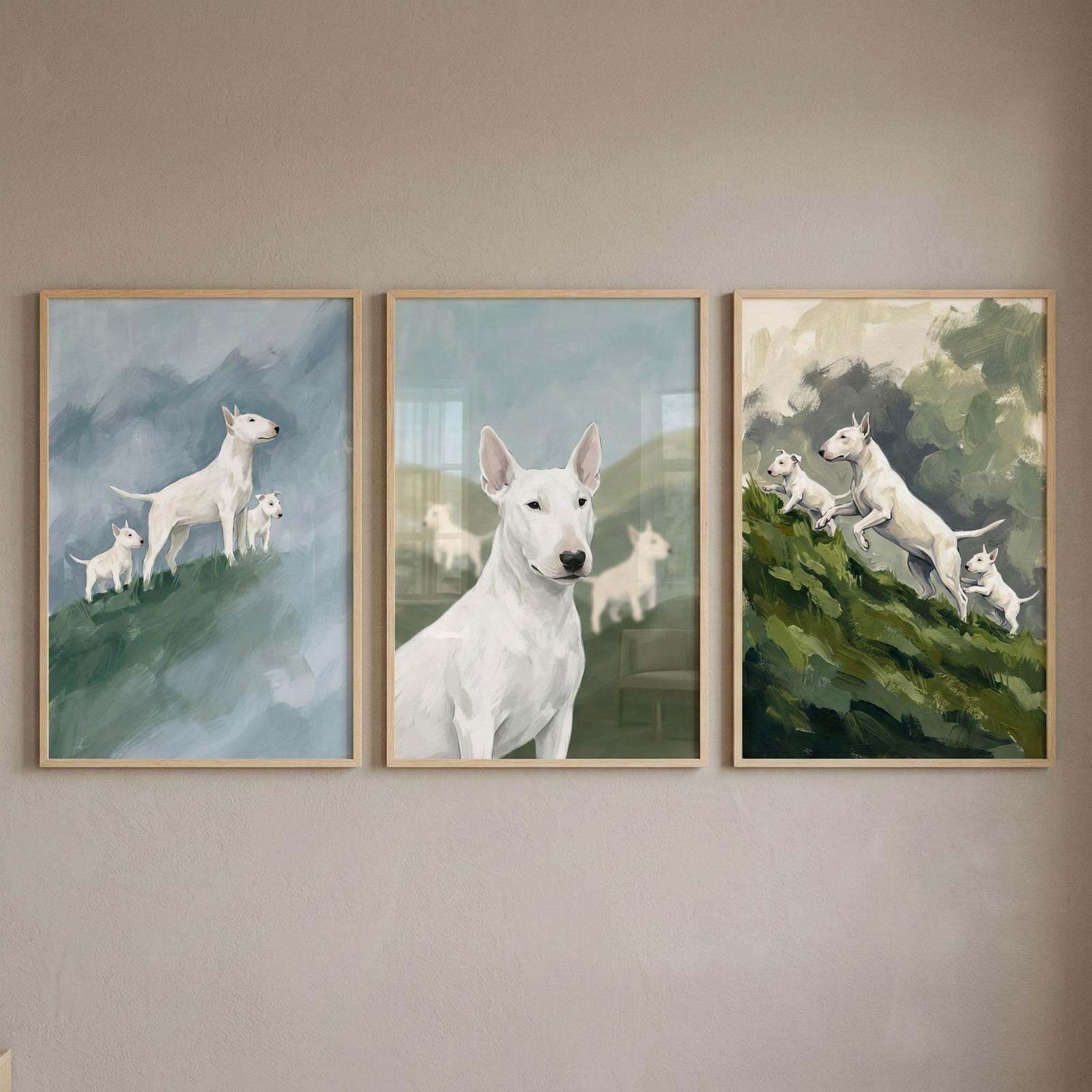 Three framed artworks hanging side-by-side on a light beige wall. Each piece features white Bull Terriers in an artistic style with visible brushwork. The left artwork shows a large dog and two puppies on a green hill under a blue-gray sky. The center piece is a close-up portrait of a white dog with a soft-focus background of more dogs in a field. The right artwork depicts three dogs running up a green slope. All three are housed in simple, light wood frames.