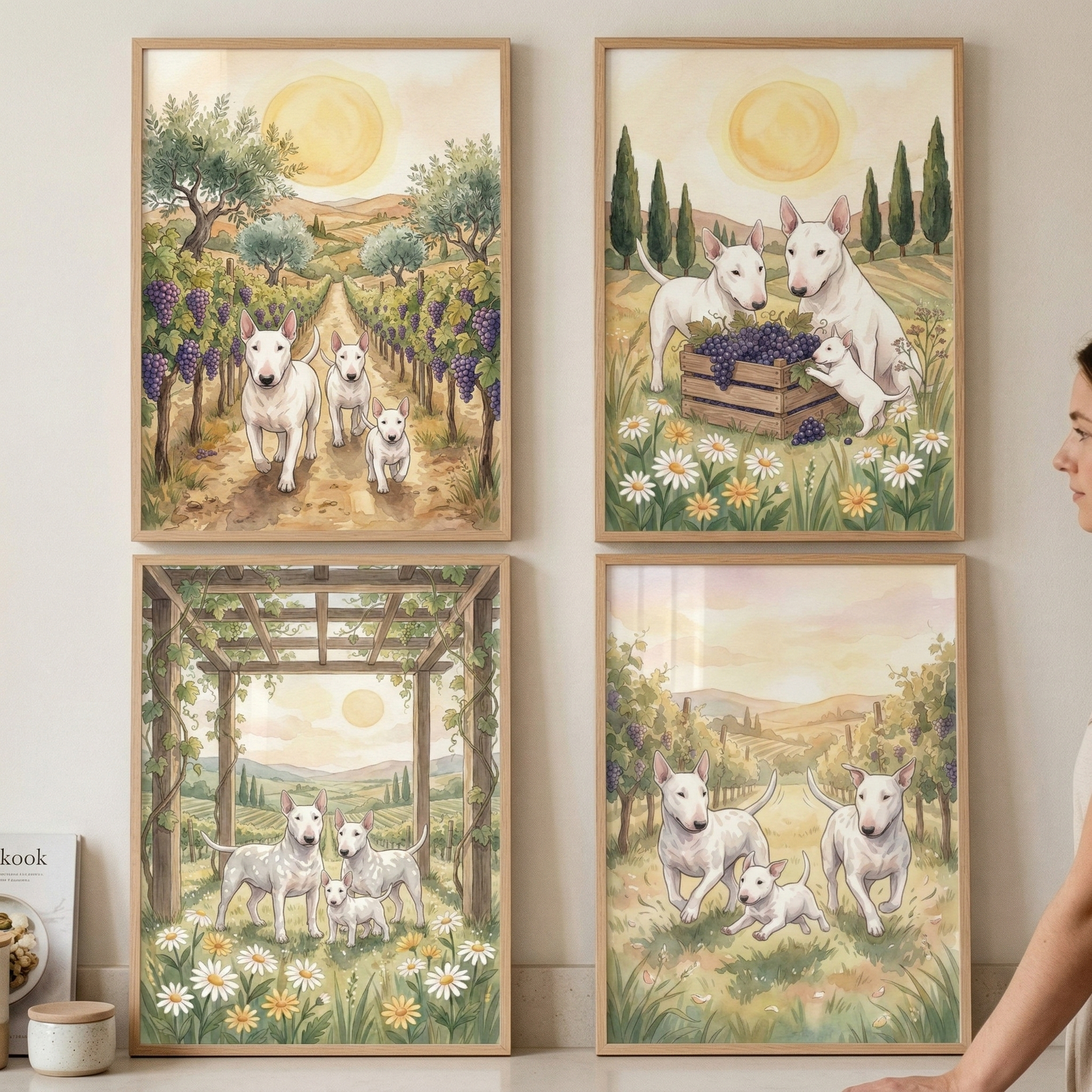 Four light-wood framed illustrations are displayed in a two-by-two grid on a plain wall. The artworks feature white terrier dogs with unique elongated heads in various pastoral vineyard settings. In the top-left, three dogs walk down a dirt path lined with grapevines under a soft sun. The top-right shows dogs with a wooden crate of grapes amidst wildflowers. The bottom-left depicts dogs standing under a wooden pergola, while the bottom-right shows them running through a grassy field. 