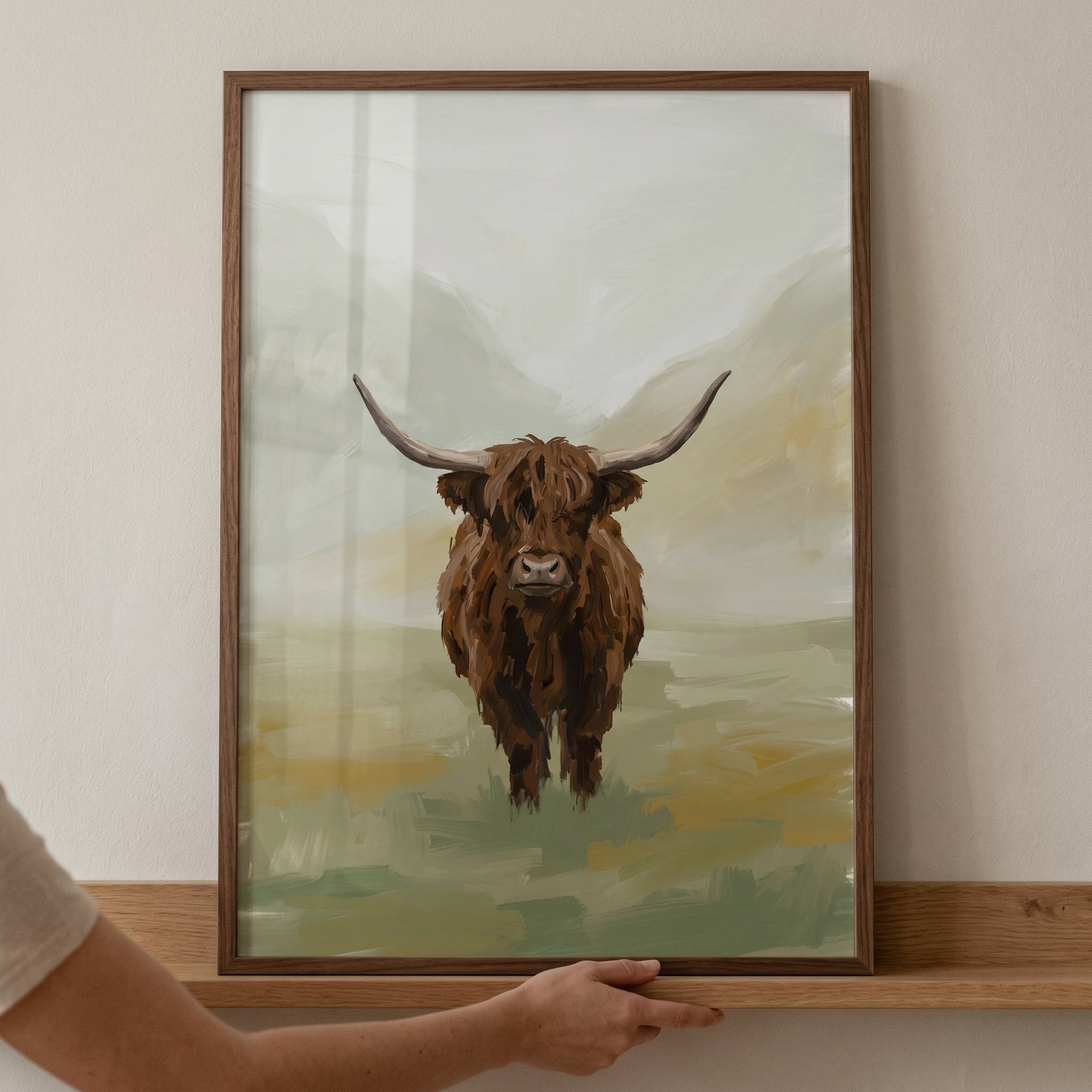 Textured brown highland cow wall art in a dark wood frame held above a wooden ledge against a plain wall.