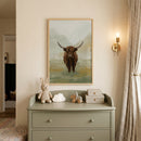 Textured brown highland cow wall art above a sage dresser with a plush bunny, cloud light, and a brass wall sconce.