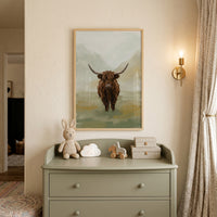 Textured brown highland cow wall art above a sage dresser with a plush bunny, cloud light, and a brass wall sconce.