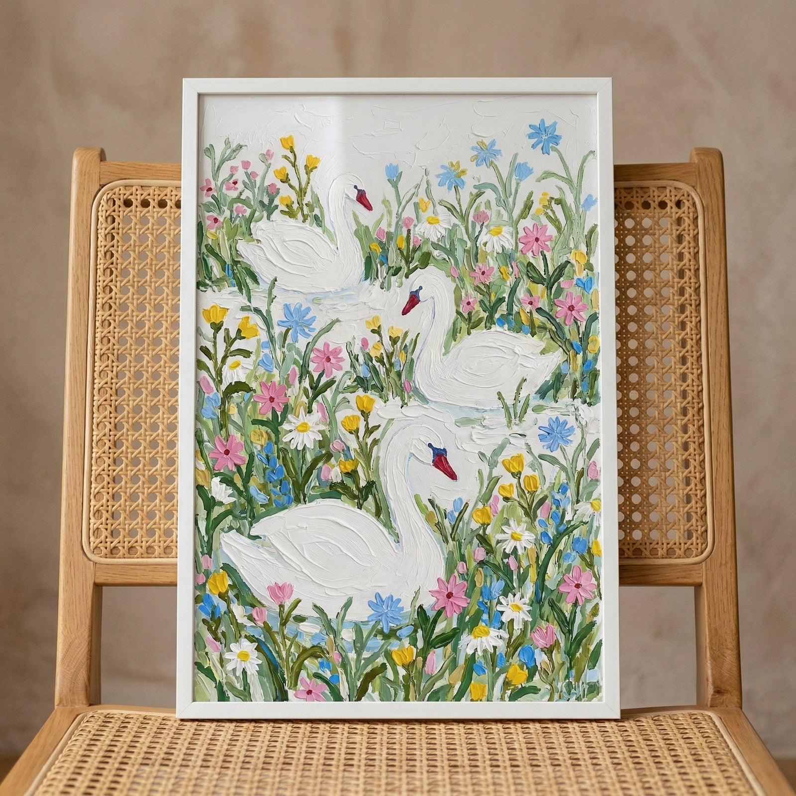 Framed painting of three white swans swimming among colorful wildflowers in soft pastel tones, displayed on a woven rattan chair. The textured brushstrokes and gentle palette create a whimsical and calming feel suited for a nursery or child’s room.