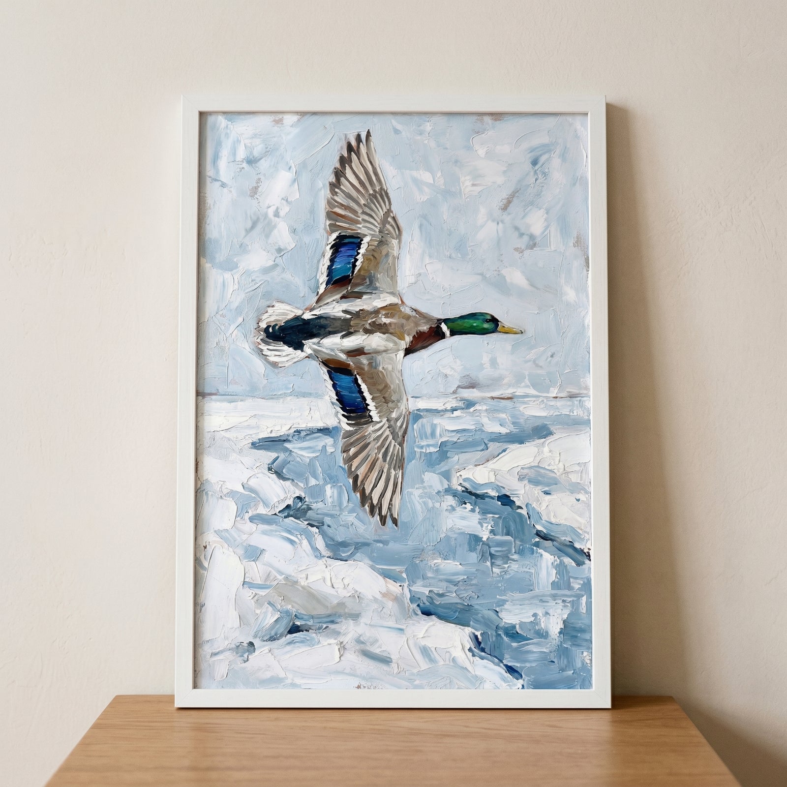 Textured winter mallard duck wall art depicts a bird in flight over icy blue water, displayed in a white frame.