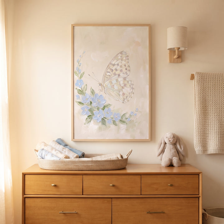 Thick impasto floral butterfly wall art hangs above a wood dresser and plush rabbit in a neutral nursery.