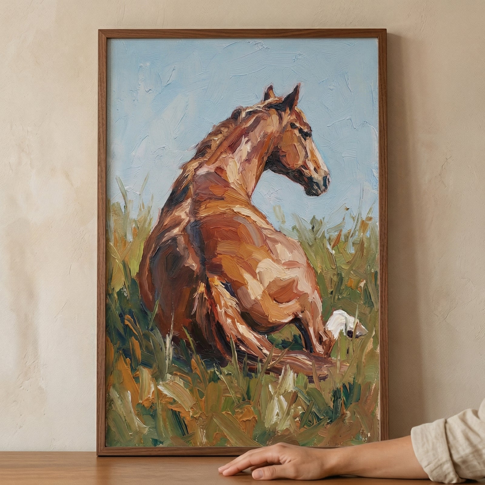 An expressive piece of art captures a chestnut horse in a relaxed pose, reclining in a meadow of tall grass. The animal is viewed from behind, turning its head to look over its shoulder. The piece is created with a thick, textured technique, using visible strokes to define the horse's form in shades of brown, ochre, and cream. 
