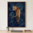 A framed piece of wall art hangs on a light wall above a wooden desk. The art features a tiger seen from behind, looking back over its shoulder. The tiger’s tail is curled into a distinctive spiral. The background is composed of glowing, light blue wavy, topographic-style lines over a dark blue base. On the desk below sits a small potted succulent in a gray cement container, a closed silver laptop, and a brown leather journal, creating a clean and modern workspace.
