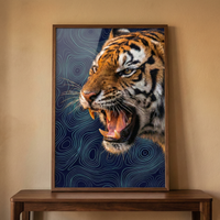 A framed artwork of a roaring tiger hangs on a dark navy wall with classic molding. The tiger is shown in profile with its mouth open, set against a dark background with intricate, light blue swirling patterns. Below the frame is a wooden desk holding a brass gooseneck lamp, a row of books, a leather desk mat, a gold-toned pencil holder, a ceramic mug, and a small abstract grey sculpture atop another stack of books. The overall scene is elegant and powerful.