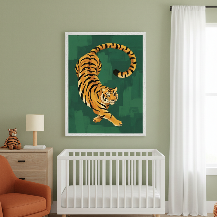 Modern nursery with sage green walls. A large framed illustration of an orange tiger stretching on a dark green painted background hangs above a white crib. A wood dresser with a lamp and stuffed tiger sits left, with an orange armchair partially visible.