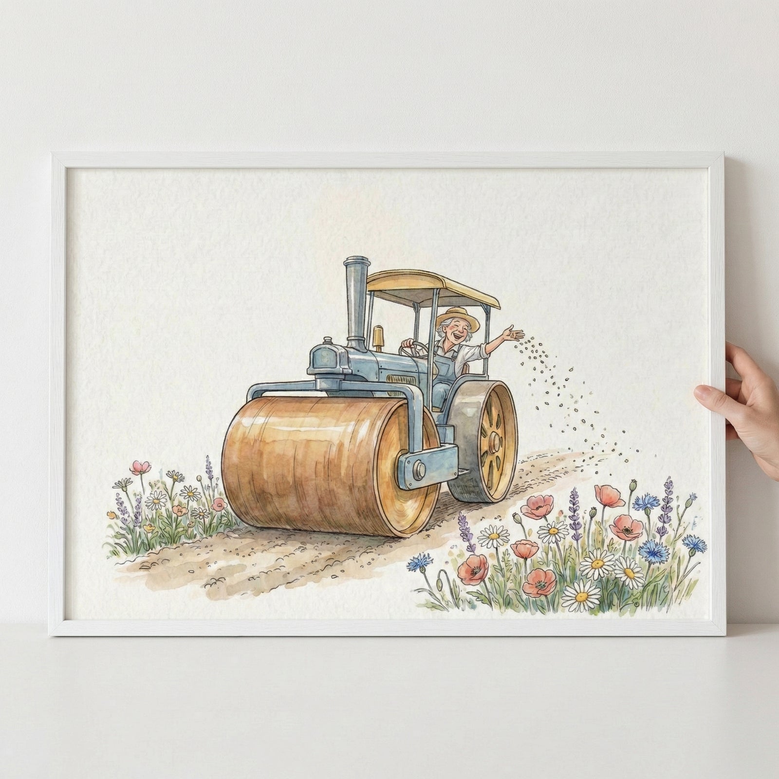 Framed watercolor painting of a smiling person driving a vintage blue tractor with large wooden rollers, scattering seeds along a dirt path surrounded by blooming wildflowers. The artwork is held up against a white wall, highlighting its soft, pastoral charm.