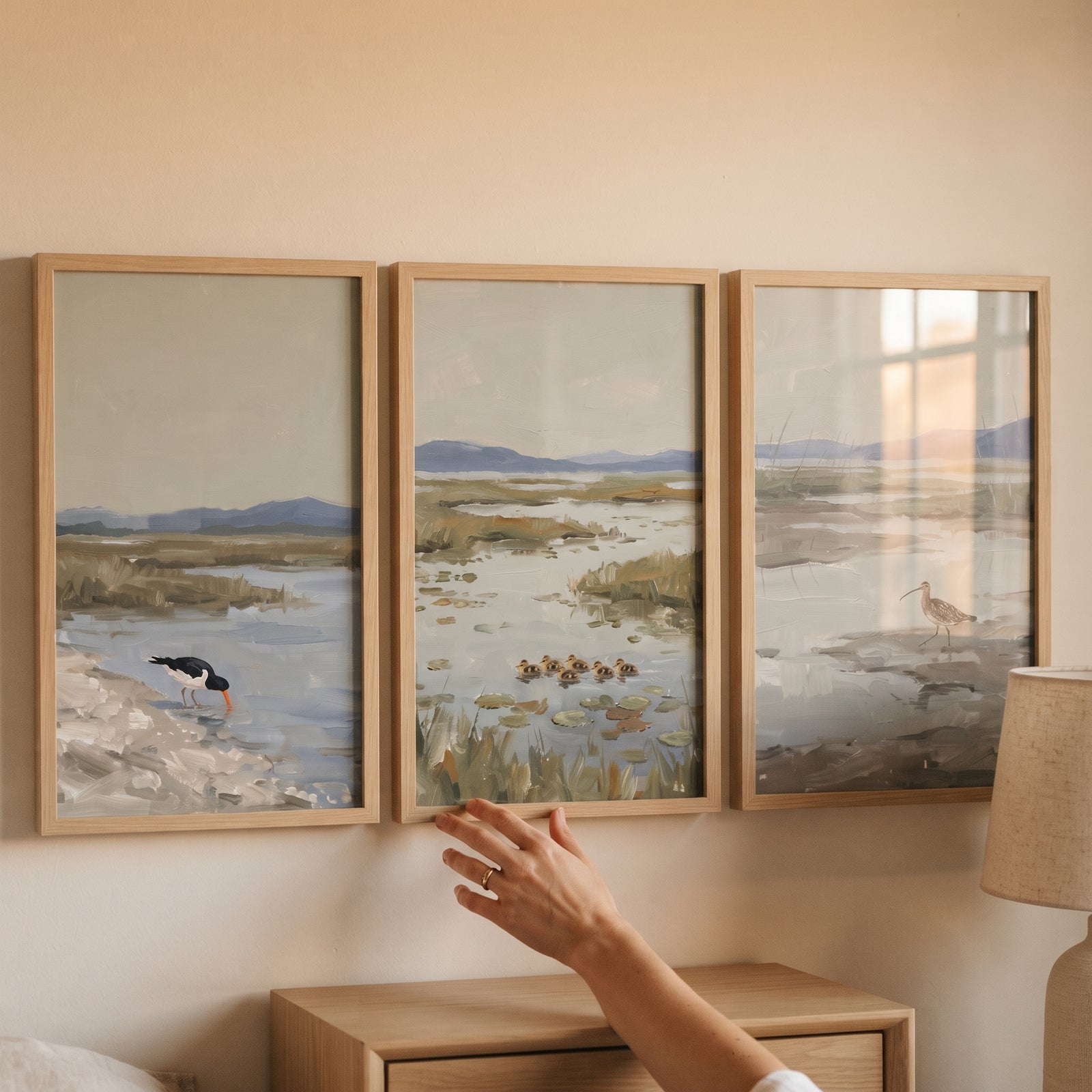A tranquil sage coastal bird wall art set of 3 hangs above a dresser, with a hand reaching toward the middle frame.
