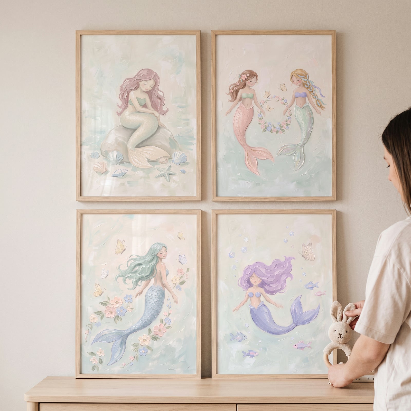 Tranquil whimsical pastel mermaid wall art set of 4 hangs in wooden frames on a wall near a person with a toy bunny.