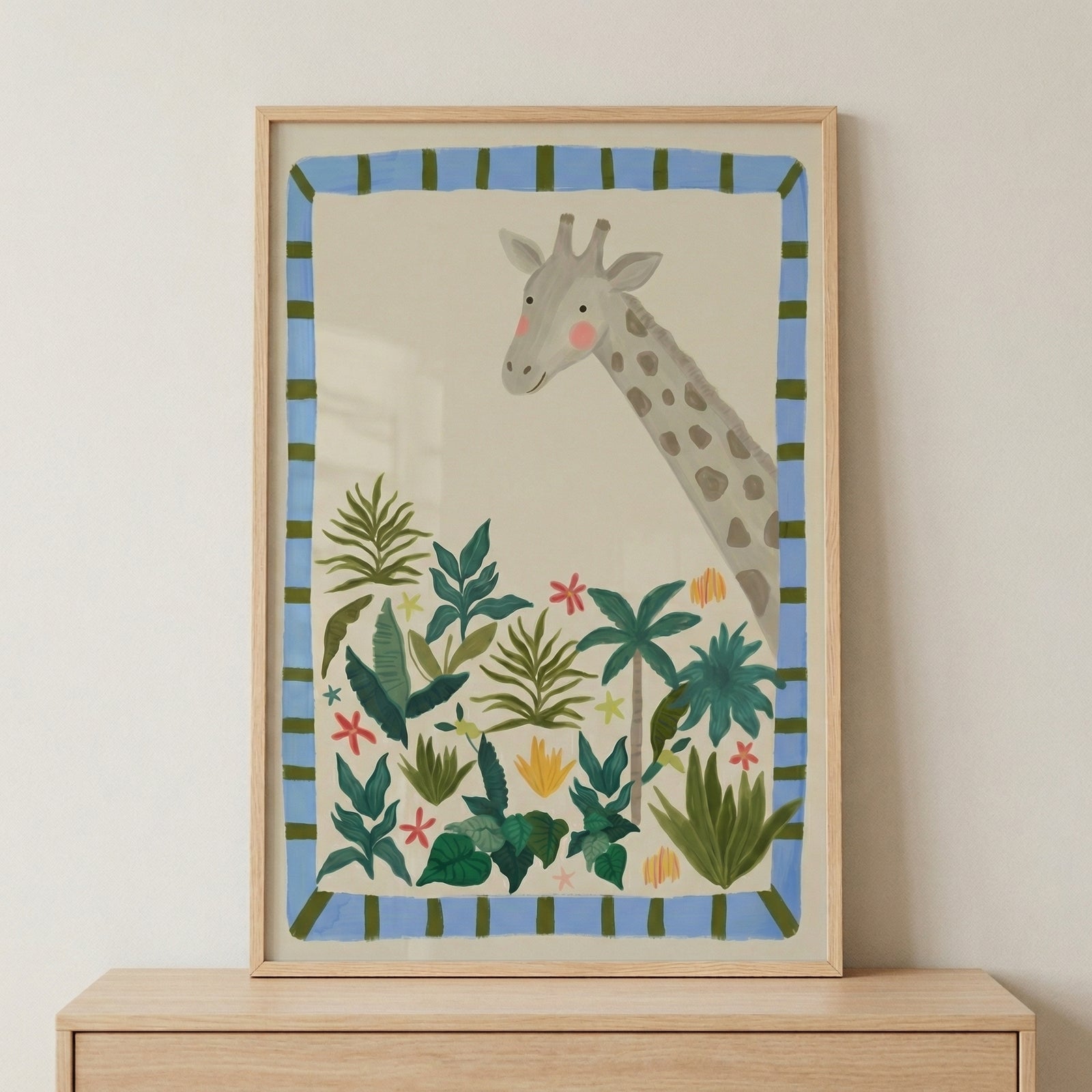 Framed illustration of a tall giraffe with a gentle expression peeking above a cluster of green tropical plants and small colorful flowers. The soft cream background and blue striped border create a playful and calming jungle themed print.