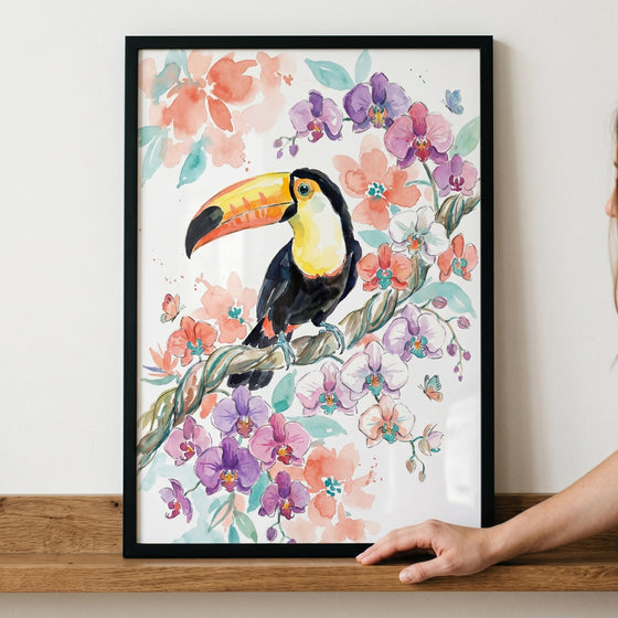 Tropical orchid branch toucan wall art in a black frame shows a watercolor bird on a floral branch on a wooden shelf.