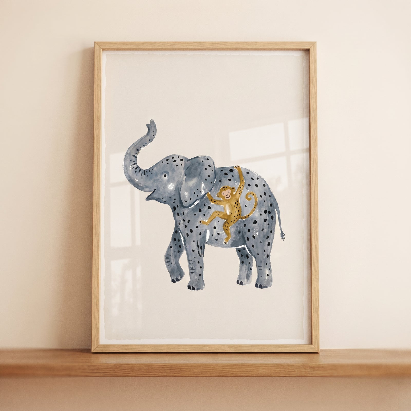 Trunk up spotted elephant wall art with a monkey, in a light wood frame leaning against a neutral wall on a shelf.