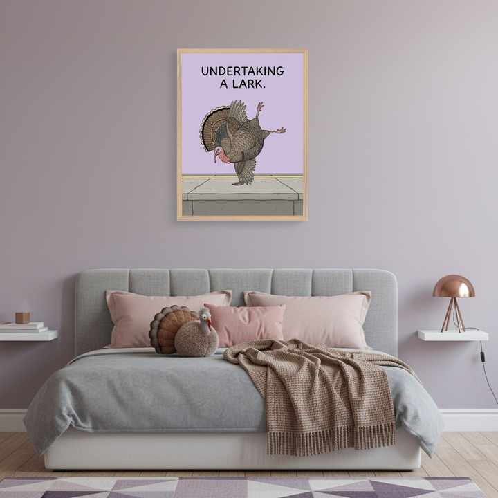 Modern bedroom with a grey upholstered bed and pink pillows. A framed print of a cartoon turkey doing a ballet pose on a curb, with the text "UNDERTAKING A LARK," hangs above the bed on a light purple wall.