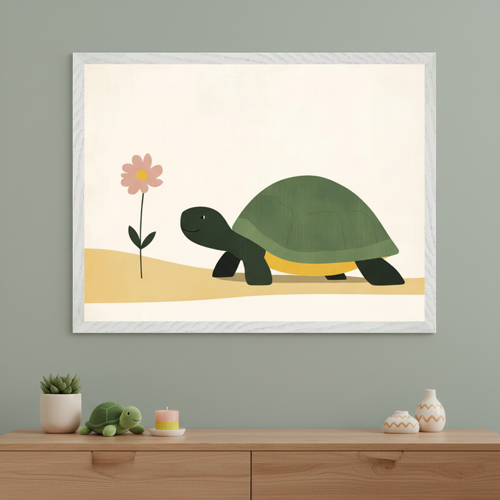 Framed illustration of a smiling cartoon turtle with a dark green shell walking past a single pink flower on a soft yellow path. The artwork hangs above a light wood dresser against a sage green wall, decorated with a plush turtle toy, a candle, a succulent, and small ceramic vases.
