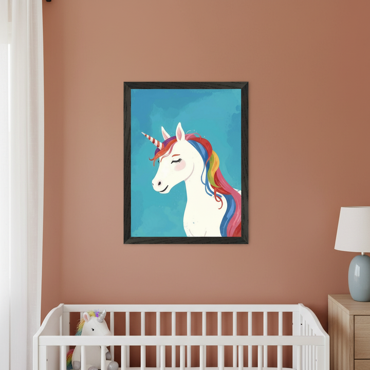 Modern nursery with a white dresser against a light blue wall. A black-framed whimsical illustration of a white unicorn with a rainbow mane and striped horn, on a blue background, hangs centered above the dresser. A unicorn figurine and pink vases with flowers are on the dresser.