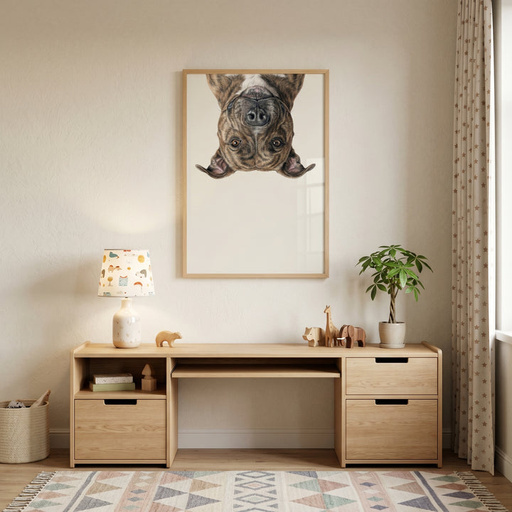 A wooden desk sits below upside down brindle dog wall art, featuring a patterned lamp, plant, and animal figurines.