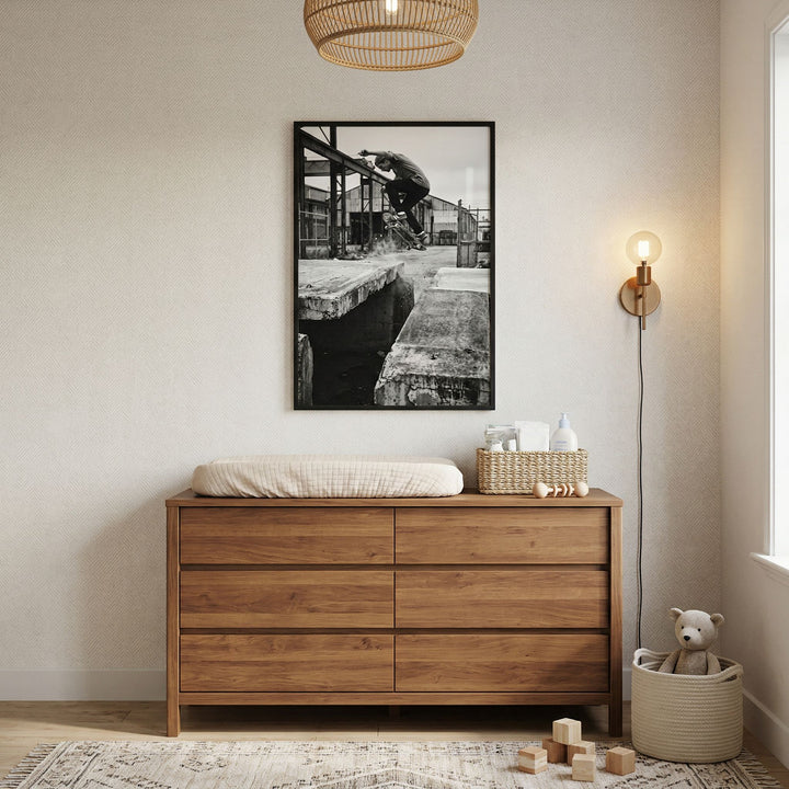 Urban street monochrome skateboarder wall art above a wooden dresser with a changing pad, lamp, and teddy bear.