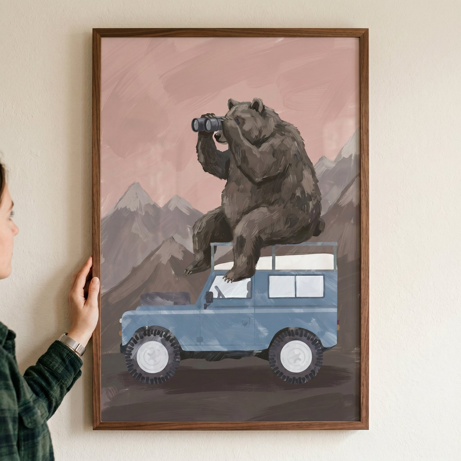 Framed using binoculars brown bear wall art shows a bear on a blue vehicle in a mountain landscape.