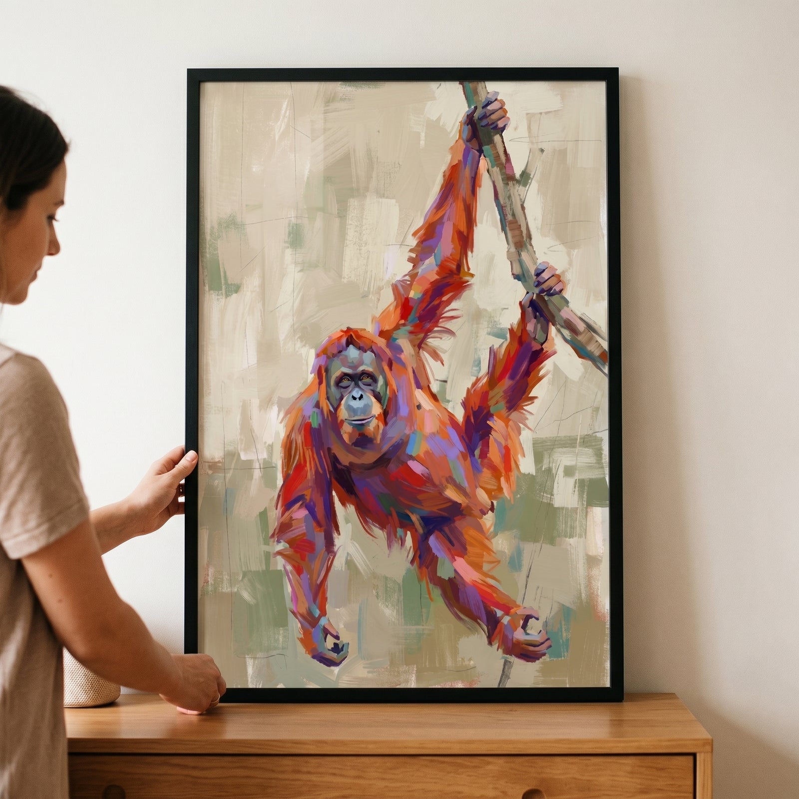 A woman holds framed vibrant palette knife orangutan wall art of a multi-colored primate hanging from a branch.