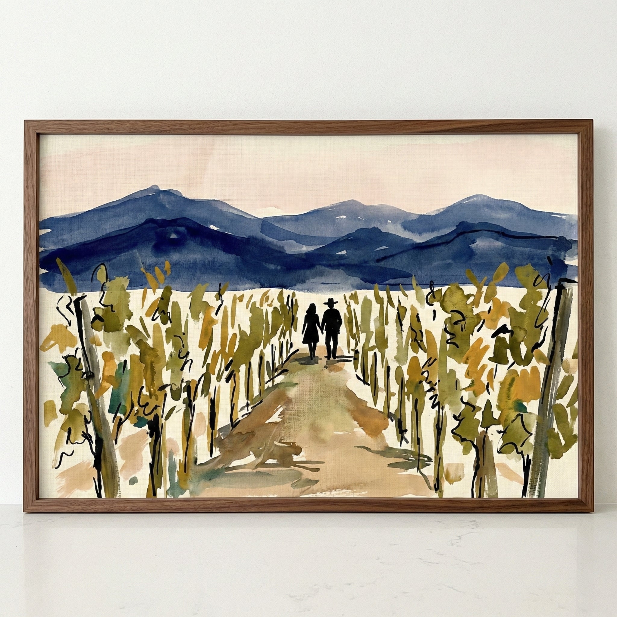 A framed piece of artwork rendered in a loose, watercolor-style showing a vineyard under a pale sky. In the foreground and middle ground, rows of grapevines with yellow and green foliage flank a central dirt path. Two dark silhouettes of a man and a woman walk hand-in-hand down the path towards the horizon. In the background, rolling mountains are depicted in shades of deep blue. The artwork is presented in a simple, dark wood frame.