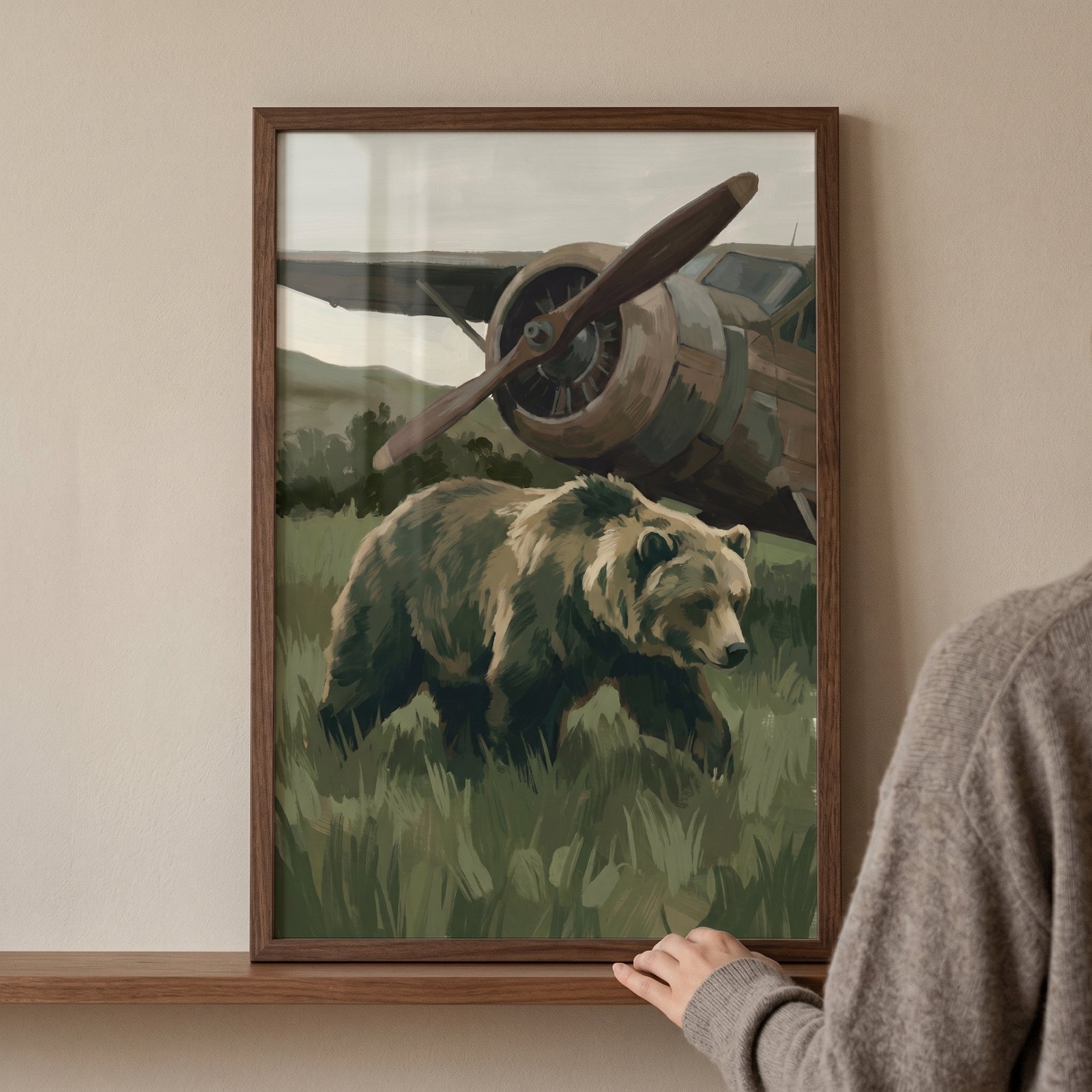 Framed vintage airplane brown bear wall art on a shelf shows a bear in tall grass in front of an old propeller aircraft.