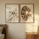 Two framed illustrations hang on a neutral wall in a bedroom setting. The left artwork features a vintage biplane flying over stylized, sepia-toned mountains. The right artwork showcases a highly detailed, close-up view of a radial aircraft engine and its propeller assembly. Both pieces share a warm, monochromatic aesthetic reminiscent of classic sketches. Below, a wooden headboard and a nightstand with a lit lamp create a cozy atmosphere centered on early aviation themes.