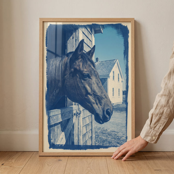 A hand holds a vintage blue stable horse wall art frame with a horse looking out of its stall and a farmhouse background.