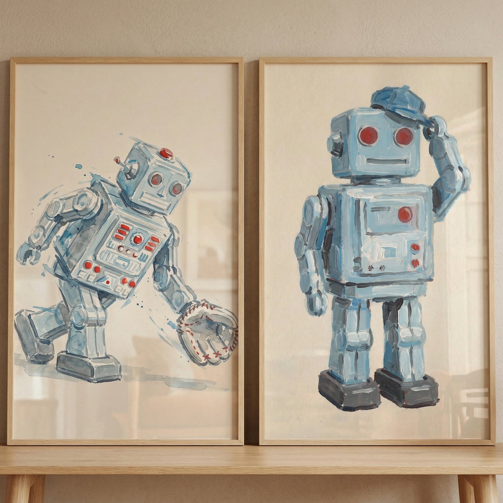 Two framed illustrations of vintage-style robots are displayed side-by-side on a light-colored wooden surface. Both pieces feature a boxy, light blue mechanical character with red circular eyes and small red button-like details on its torso. 
