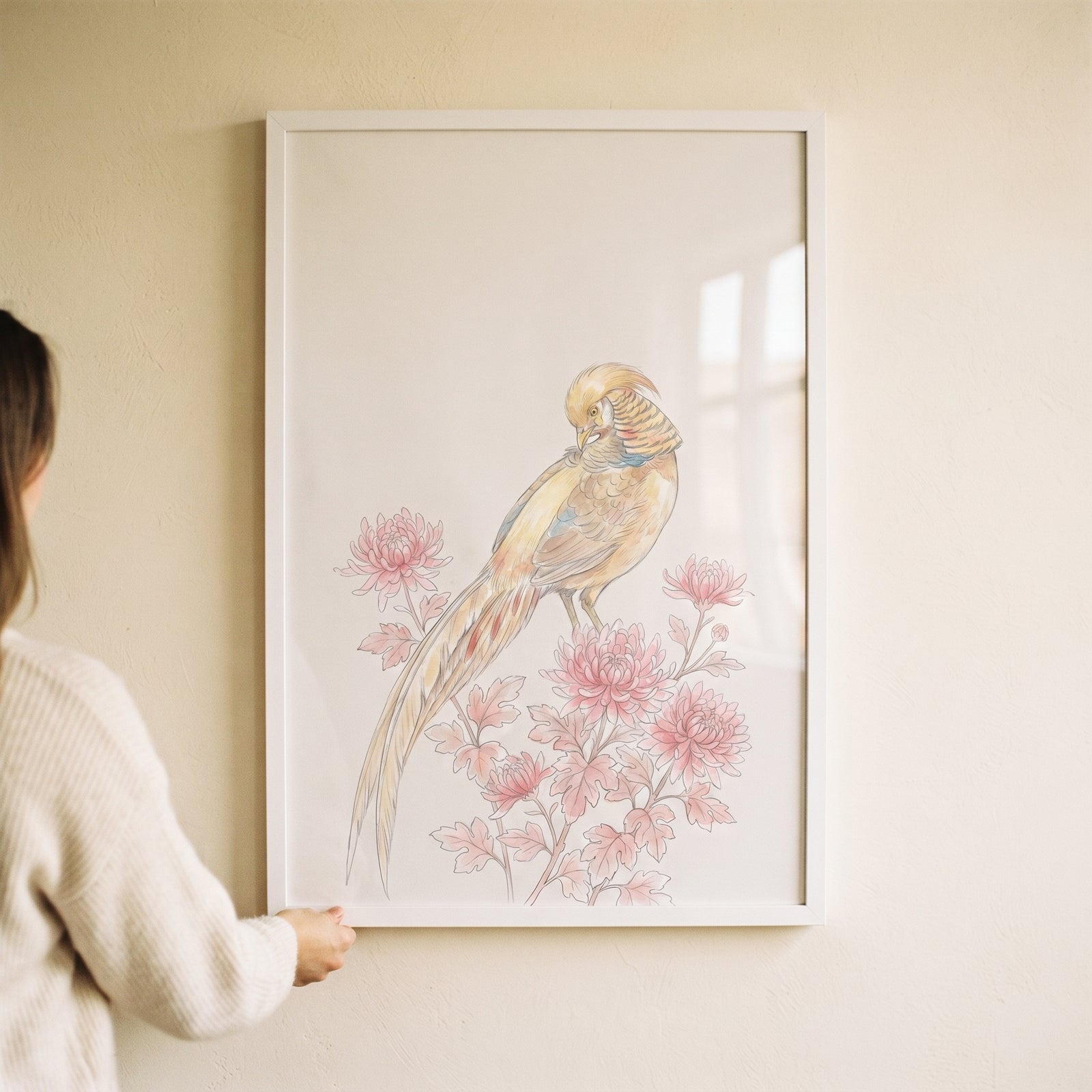 A person holds vintage chinoiserie pink pheasant wall art in a white frame, depicting a golden bird on pink flowers.