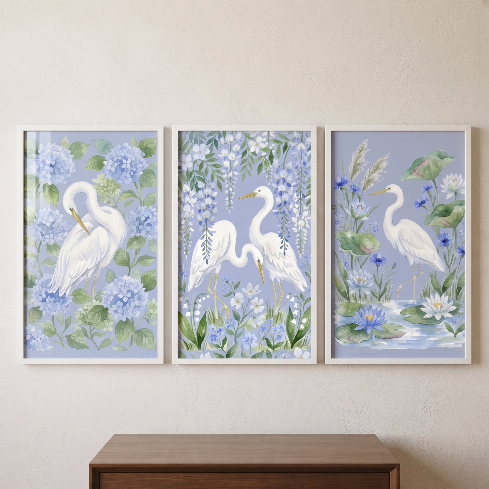 Vintage coastal white heron bird wall art set of 3 depicts birds among blue hydrangeas, wisteria, and water lilies.