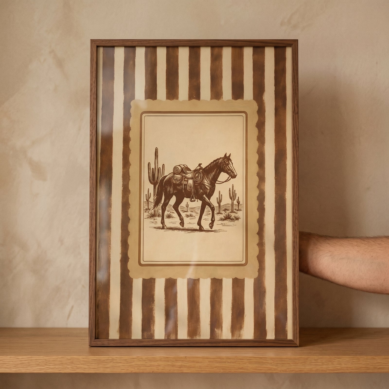 Framed vintage desert saddled horse print featuring a striped border, displayed on a wooden shelf.