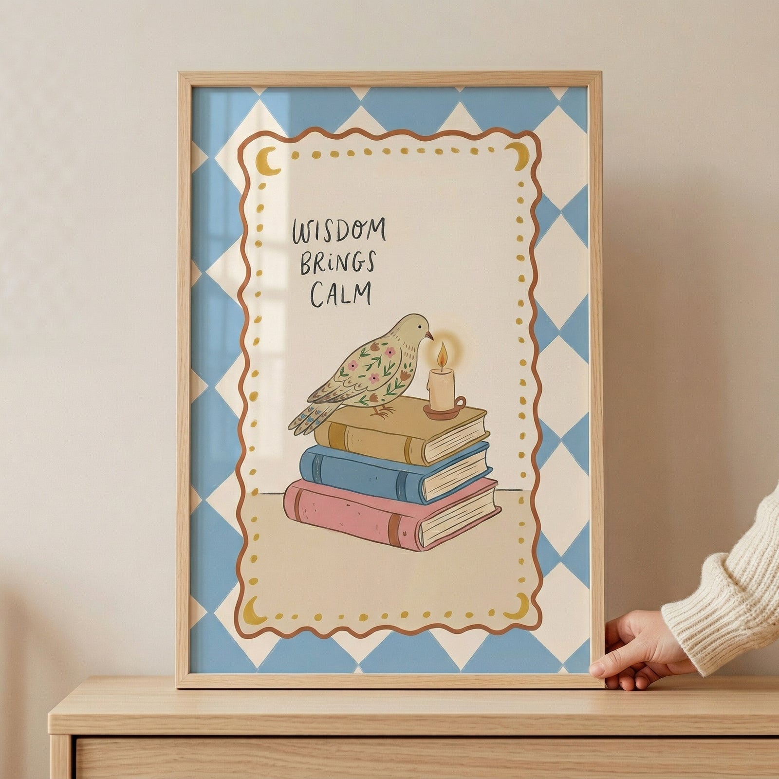 Framed illustration of a small bird perched on a stack of three books beside a lit candle, set against a blue diamond patterned background. The text "WISDOM BRINGS CALM" appears above the bird, creating a cozy and reflective reading themed print.