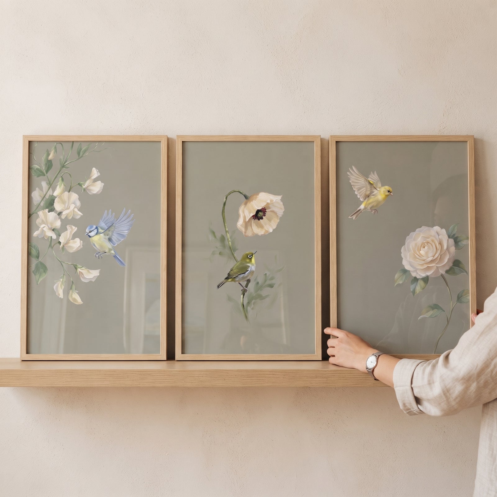 Vintage garden floral bird wall art set of 3 with birds and white flowers in light wood frames on a shelf.