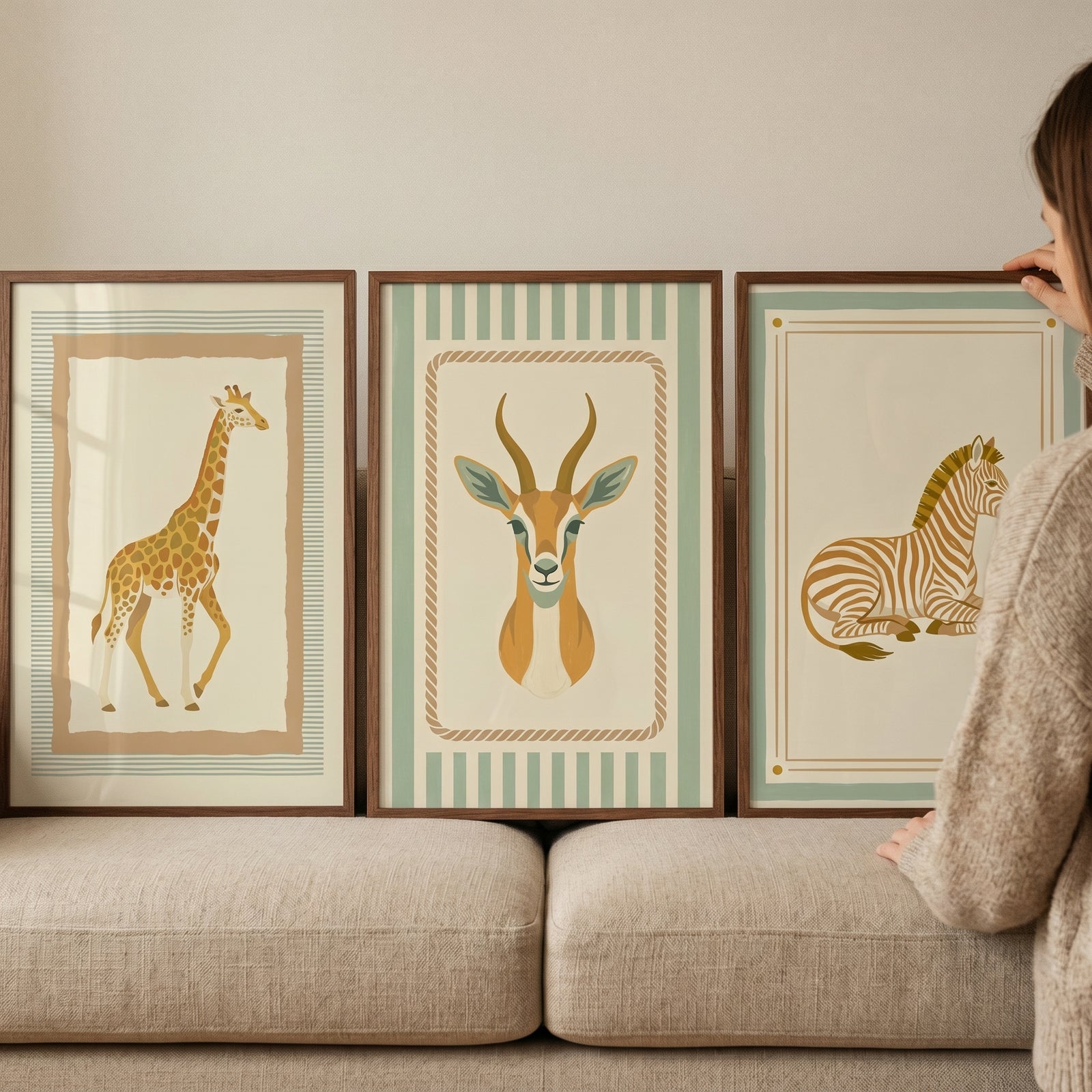 Wooden framed vintage neutral safari animal wall art set of 3 with a giraffe, gazelle, and zebra resting on a beige sofa.